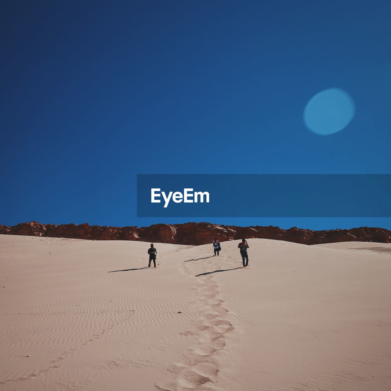 People standing on sand with sky in background