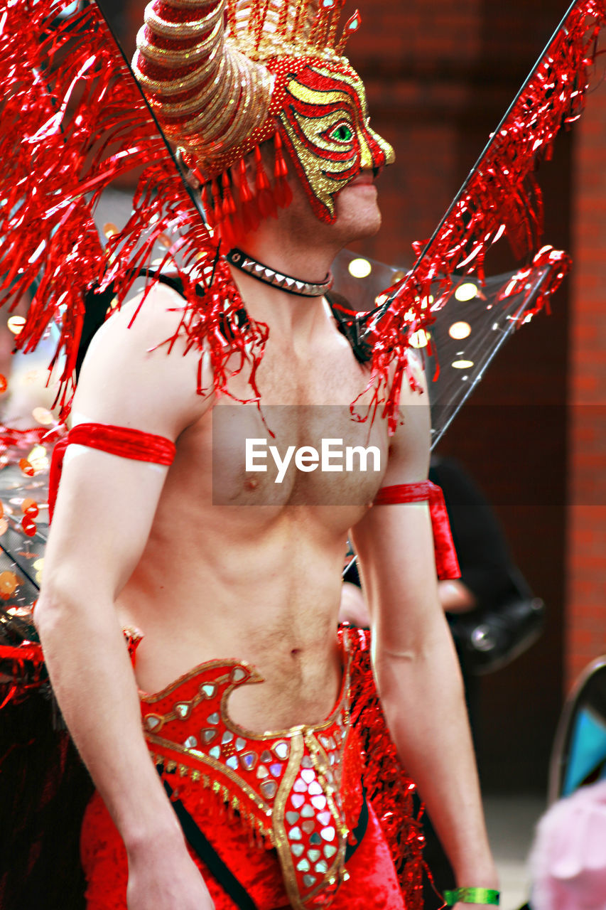 MIDSECTION OF SHIRTLESS MAN WITH RED WOMAN IN TRADITIONAL MASK