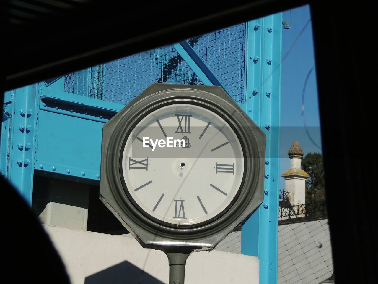 Close-up of clock by building seen through broken glass