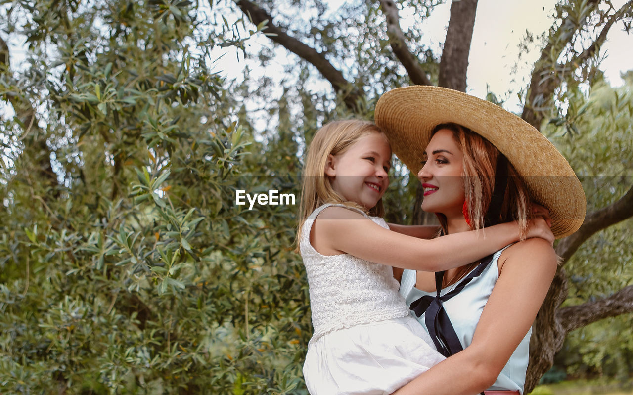 Happy mother holding daughter while standing against tree