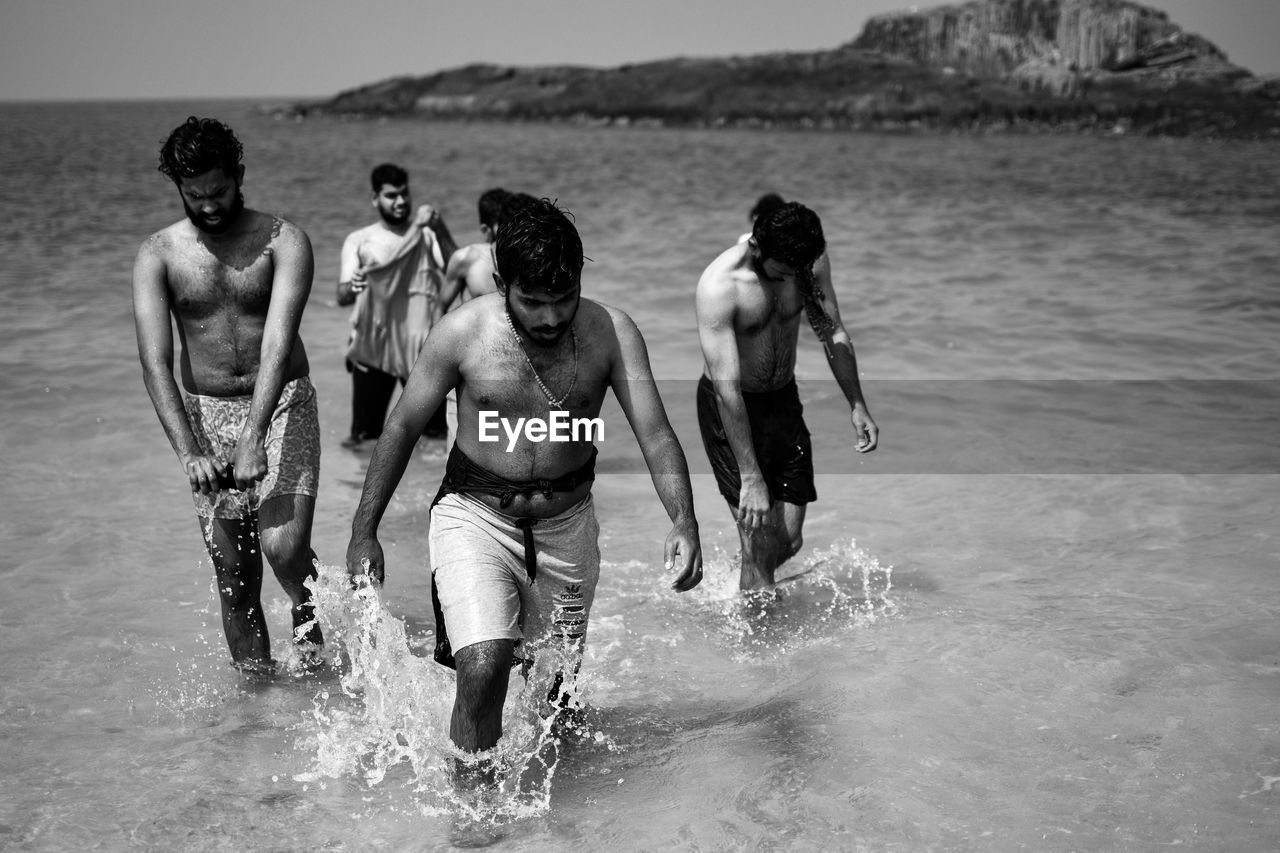 Shirtless men walking in sea