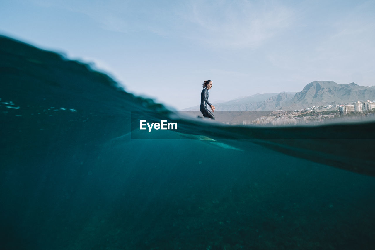 Pulled back split image of female surfer in wetsuit on a wave