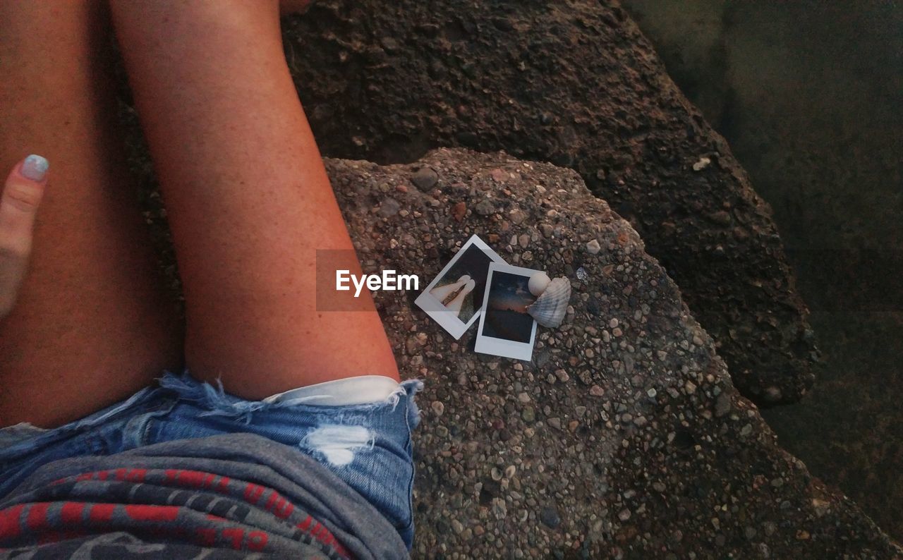 Midsection of young woman sitting with photographs on rocks