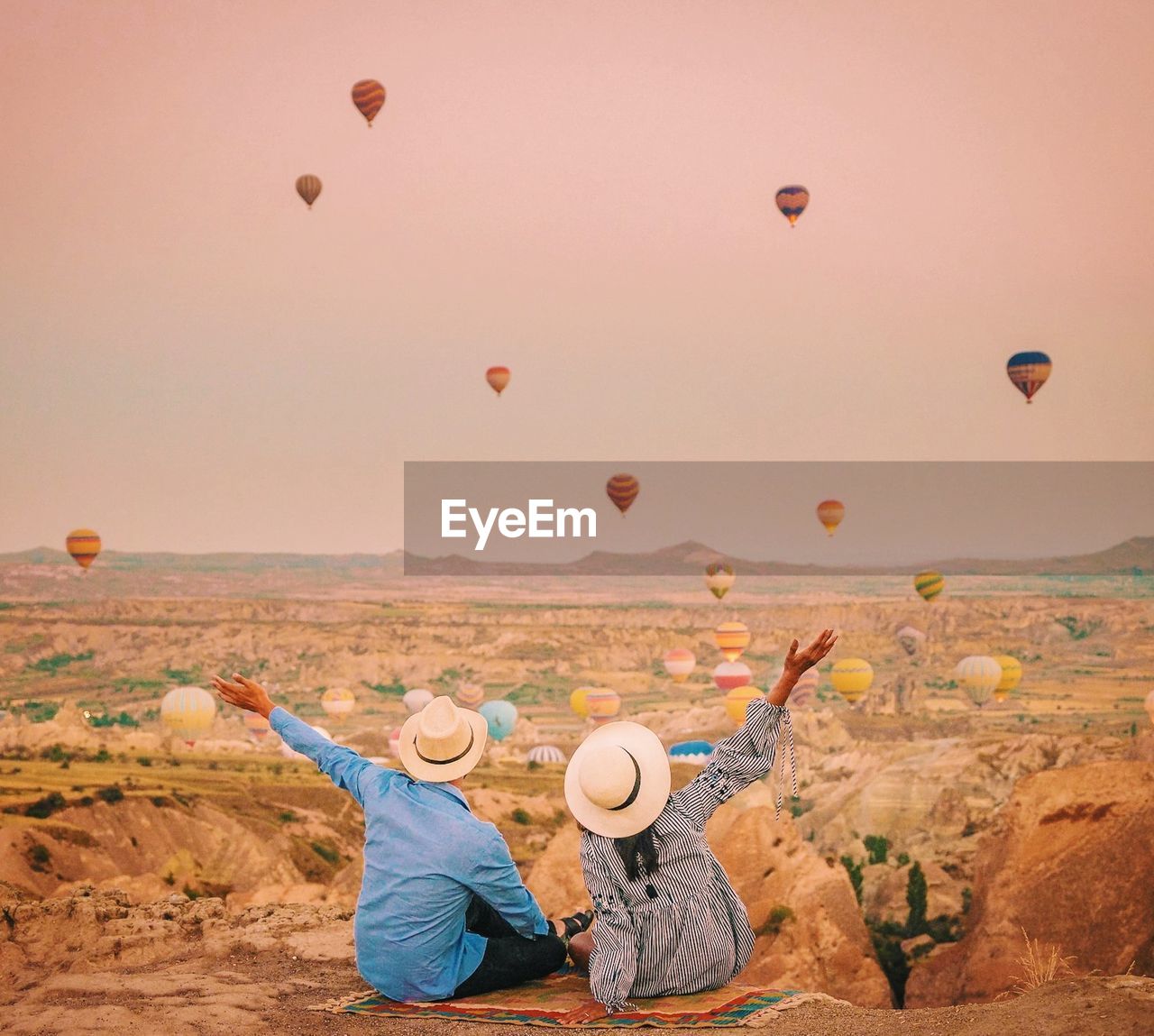 Rear view of couple looking at hot air balloons flying against sky