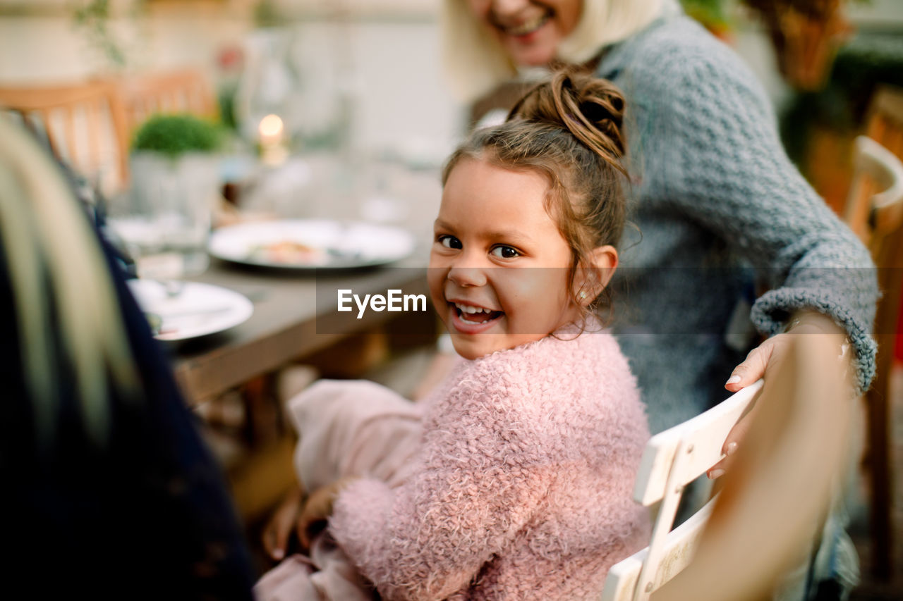 Portrait of smiling girl sitting with grandmother by dining table during lunch