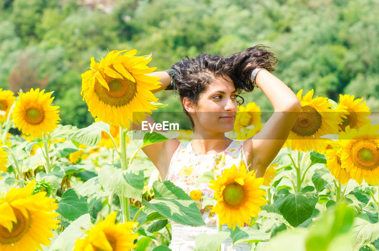 PORTRAIT OF SMILING WOMAN WITH YELLOW SUNFLOWER IN PARK