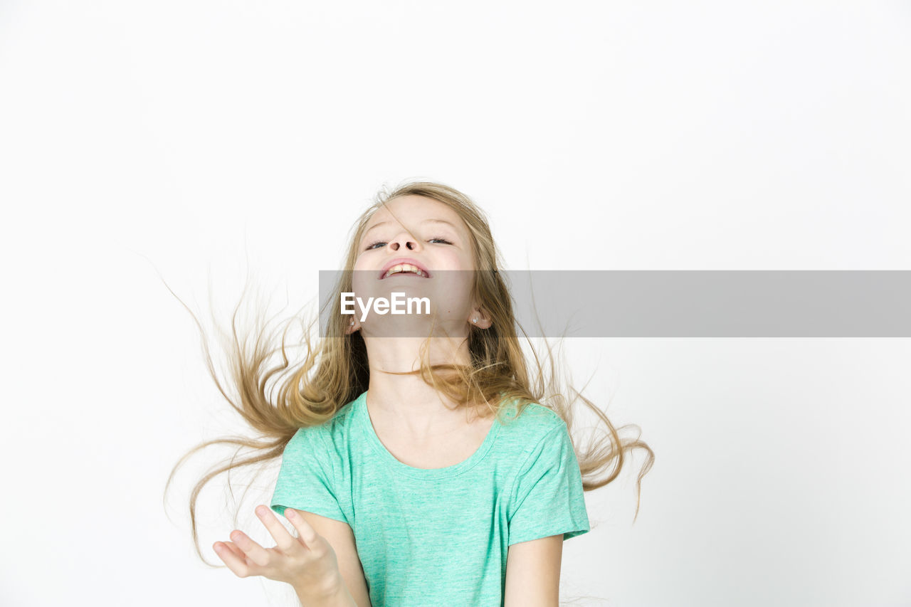 Playful girl tossing hair while standing against white background