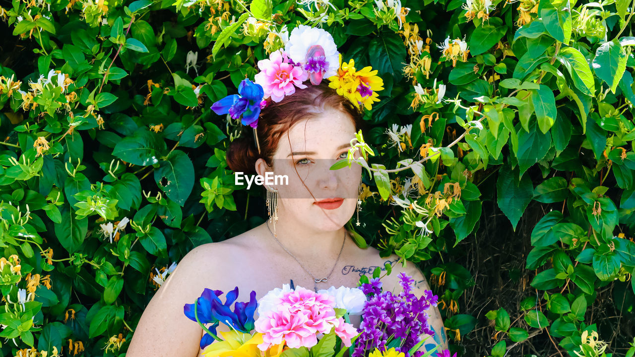 Portrait of young woman standing against plants
