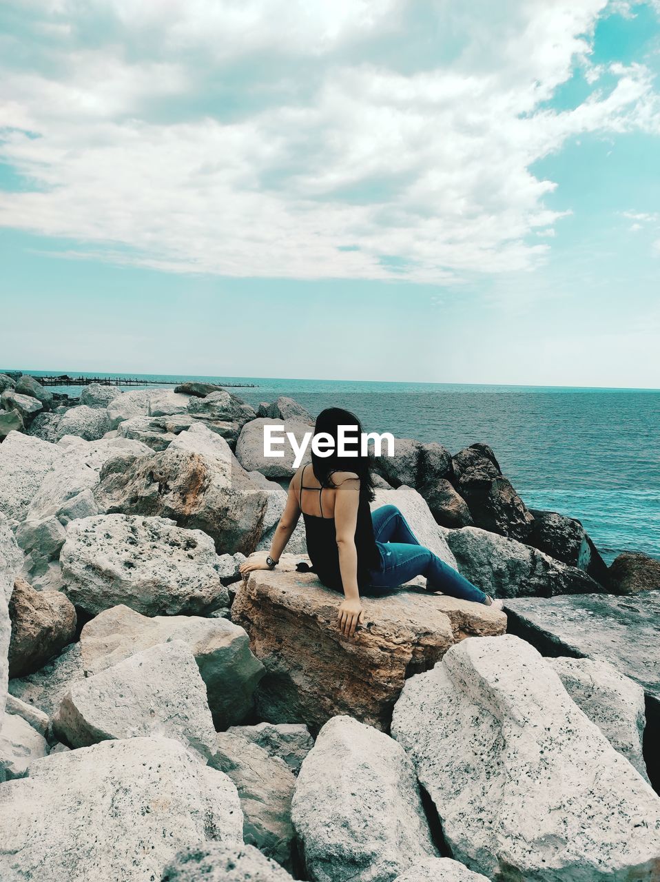 Woman sitting on rock by sea against sky