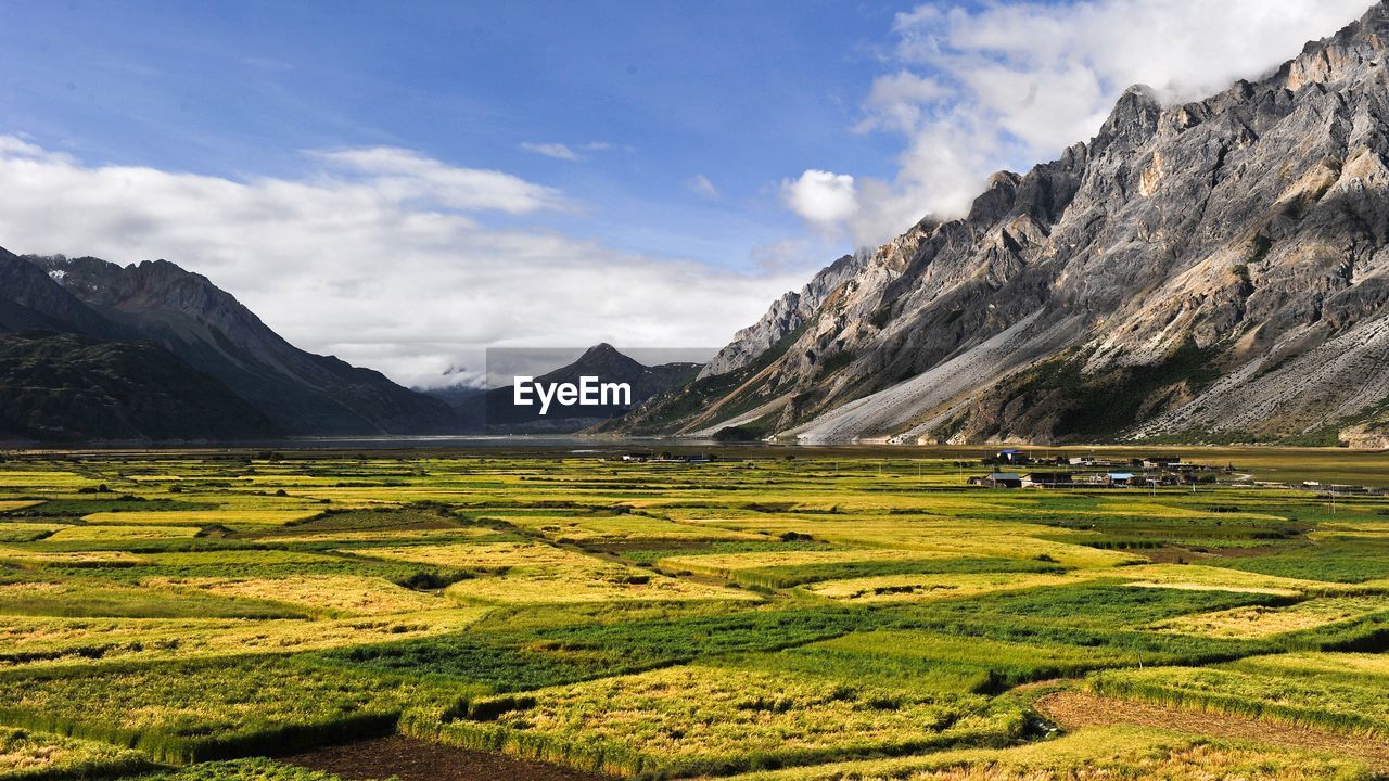 Scenic view of green field by mountains against sky