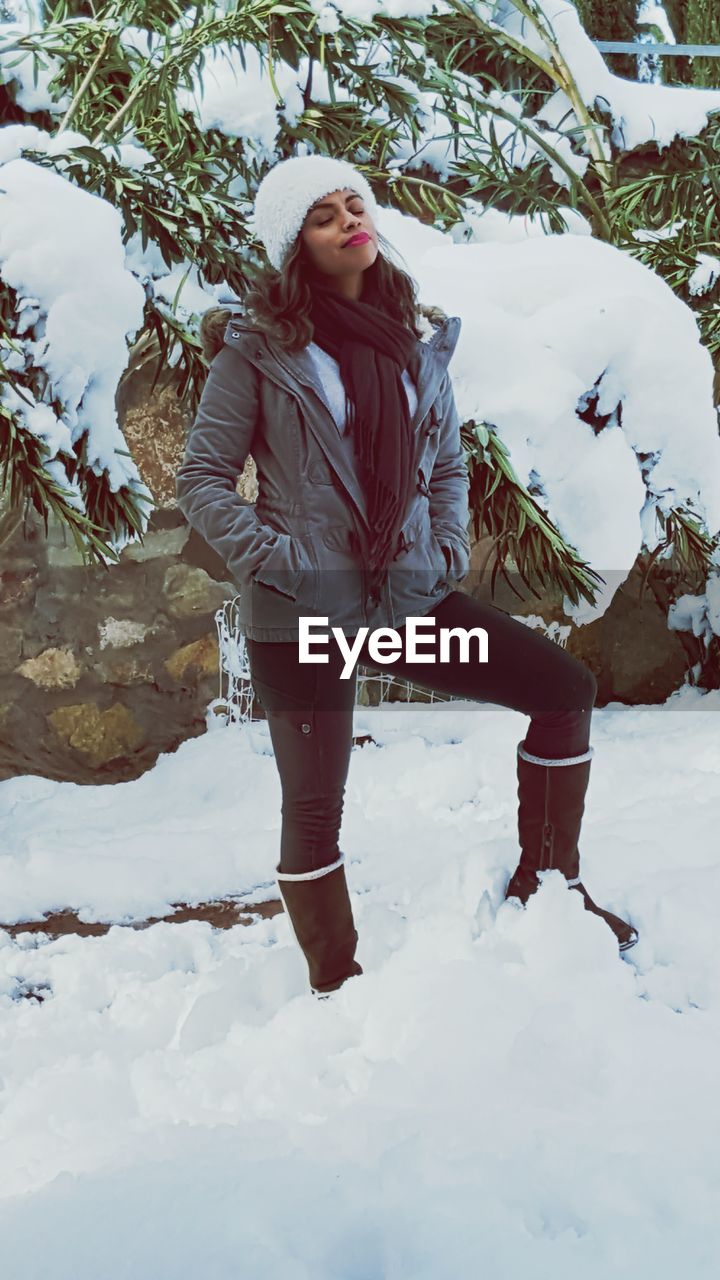 PORTRAIT OF YOUNG WOMAN STANDING ON SNOW COVERED LANDSCAPE