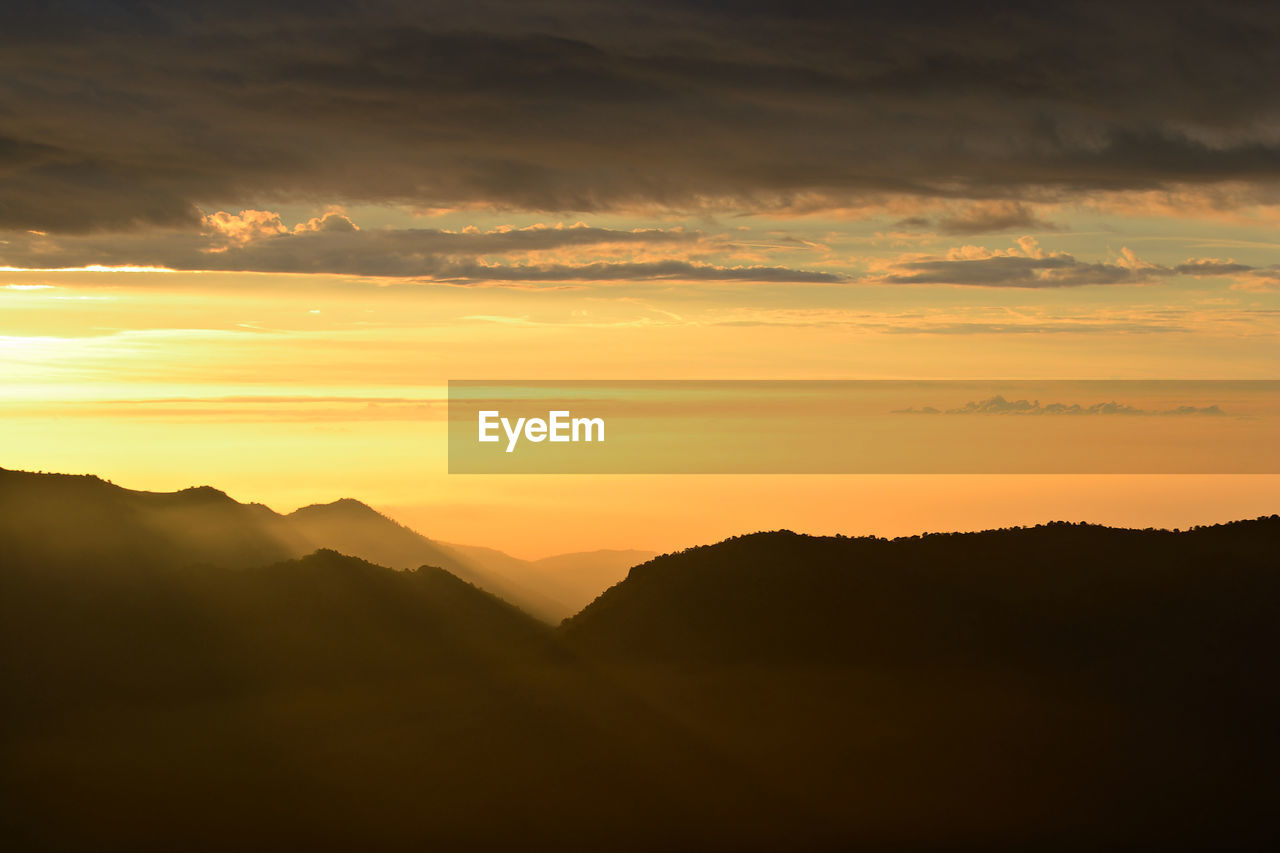 SCENIC VIEW OF DRAMATIC SKY OVER SILHOUETTE MOUNTAINS DURING SUNSET