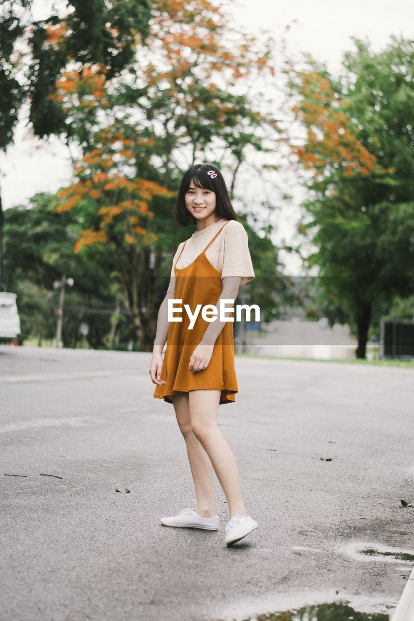 PORTRAIT OF A SMILING YOUNG WOMAN STANDING BY ROAD