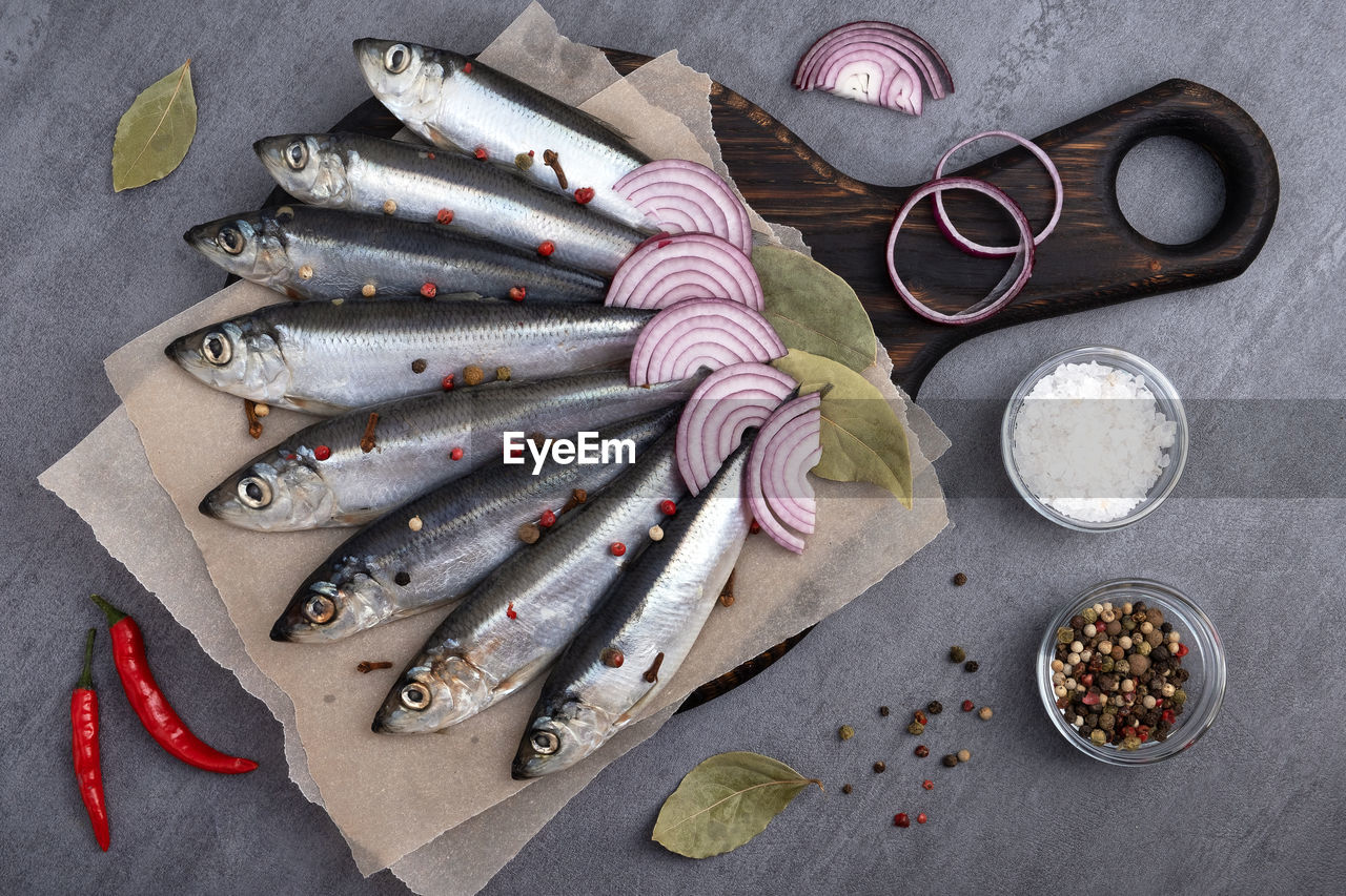 Close-up top view of several pickled herrings with spices on parchment paper on a serving board.