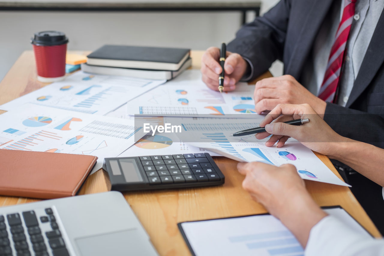 Midsection of and businessman and colleague discussing over graph on table