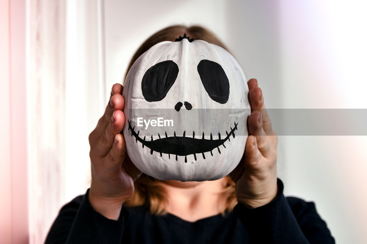 Woman holding funny pumpkin face in front of her face. halloween background diy. do it yourself.