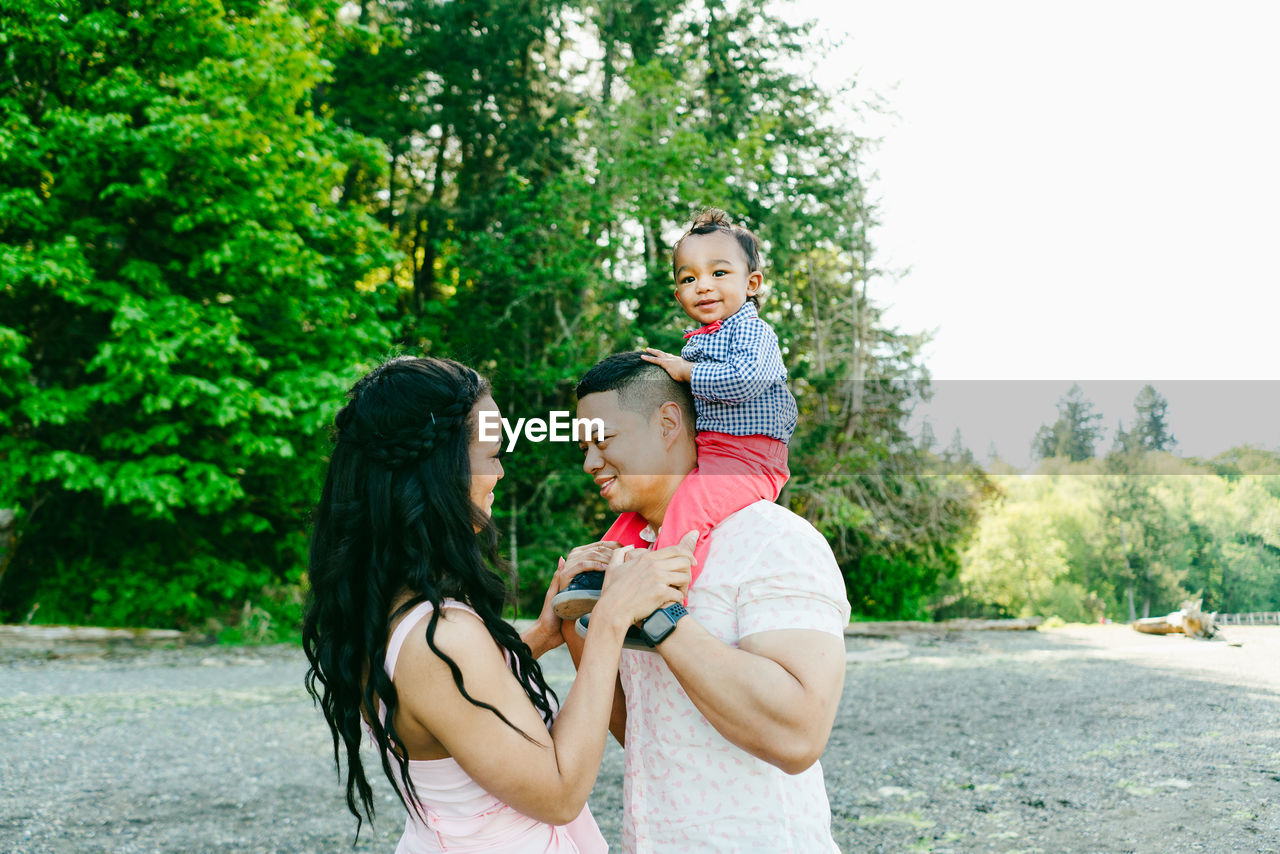 Side view of a boy sitting on his dad's shoulders while mom looks on