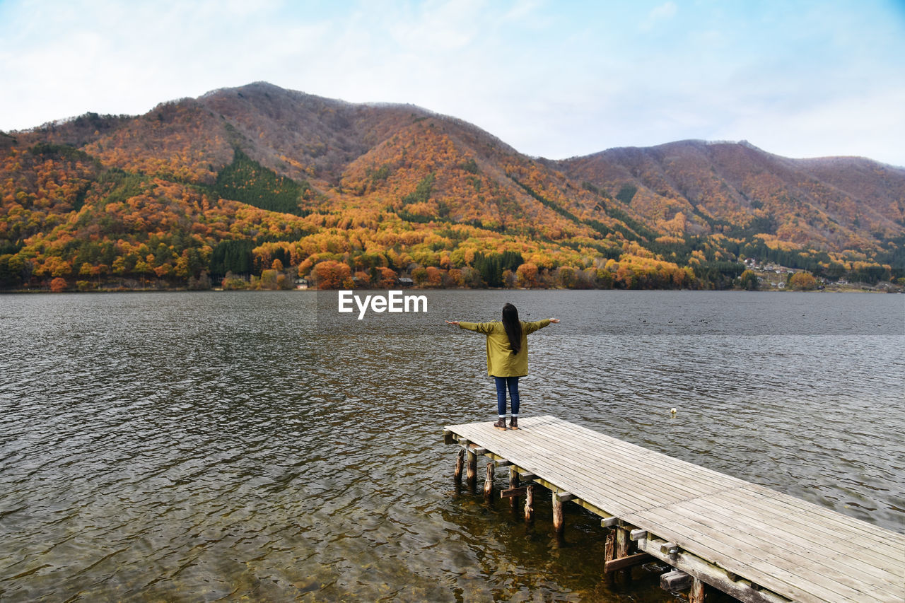 Rear view of woman standing on pier in lake against mountains