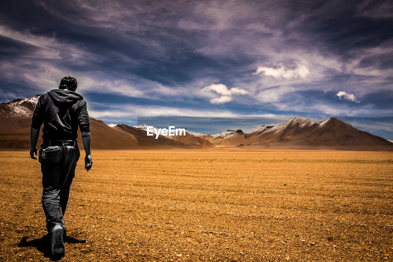 Rear view of man walking on arid landscape against sky