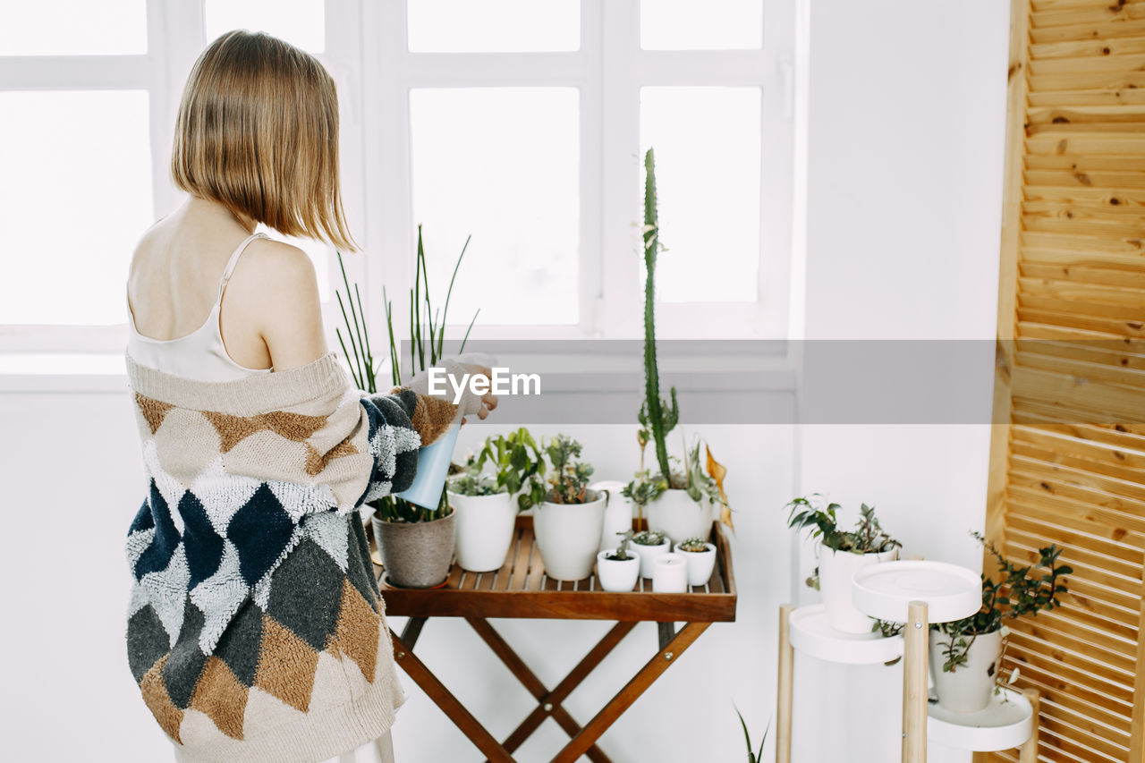 REAR VIEW OF WOMAN HOLDING POTTED PLANT