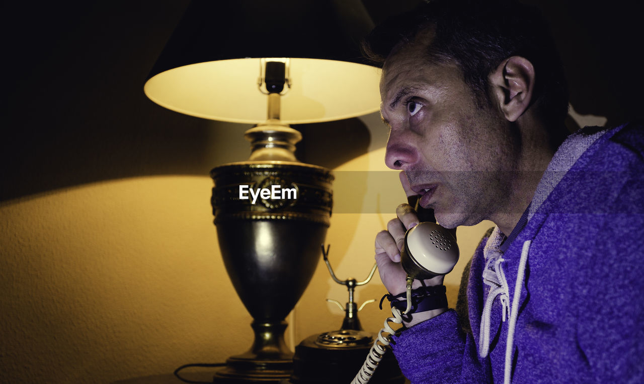 Man talking on telephone by electric lamp at home