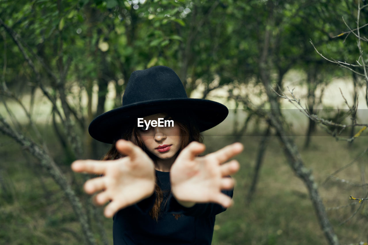 portrait of young woman wearing hat while standing against trees