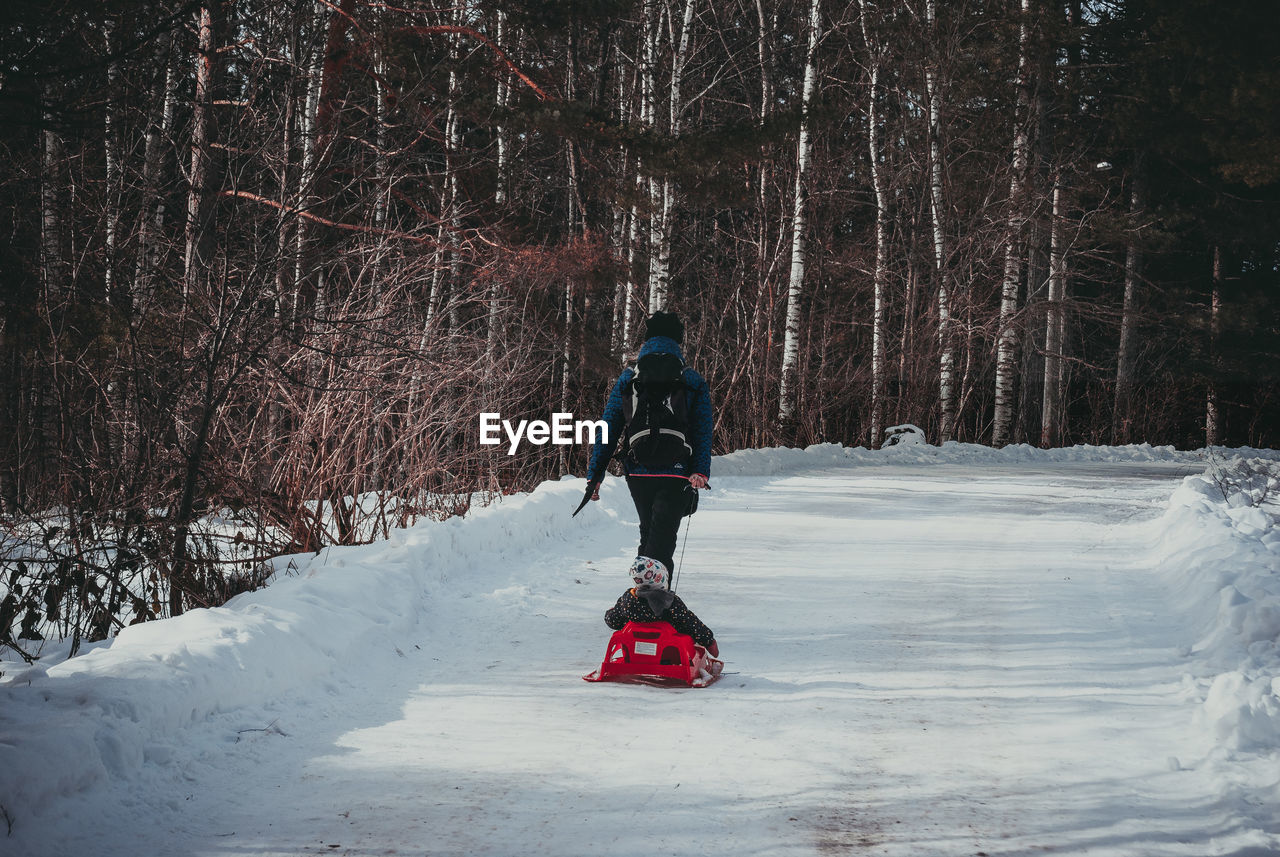 Rear view of woman with son walking on snow covered road