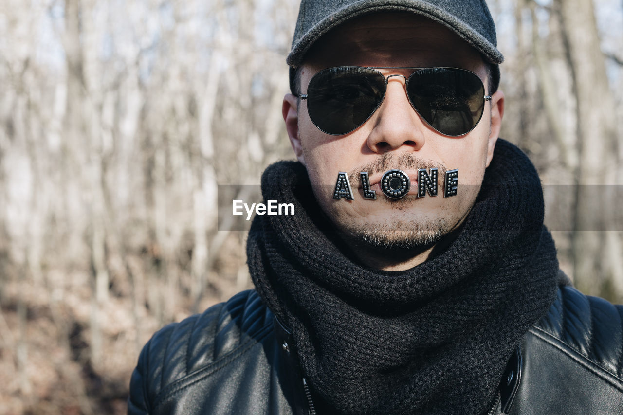 Close-up of man sunglasses with alone text on mouth at forest
