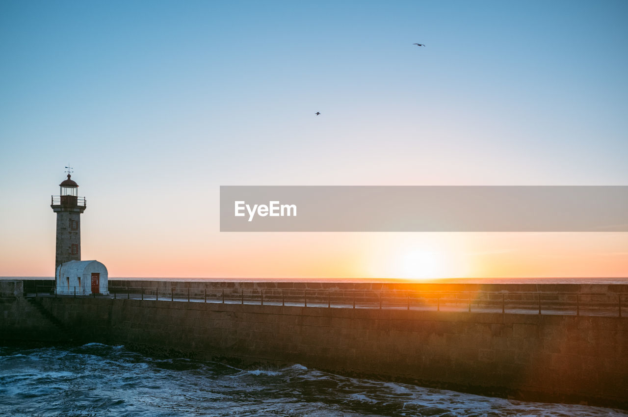 Lighthouse in sea against sky during sunset