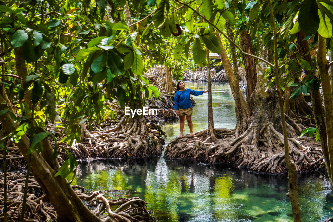 Full length of woman standing on tree in lake