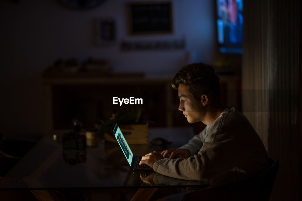 Side view of boy using laptop on table at night