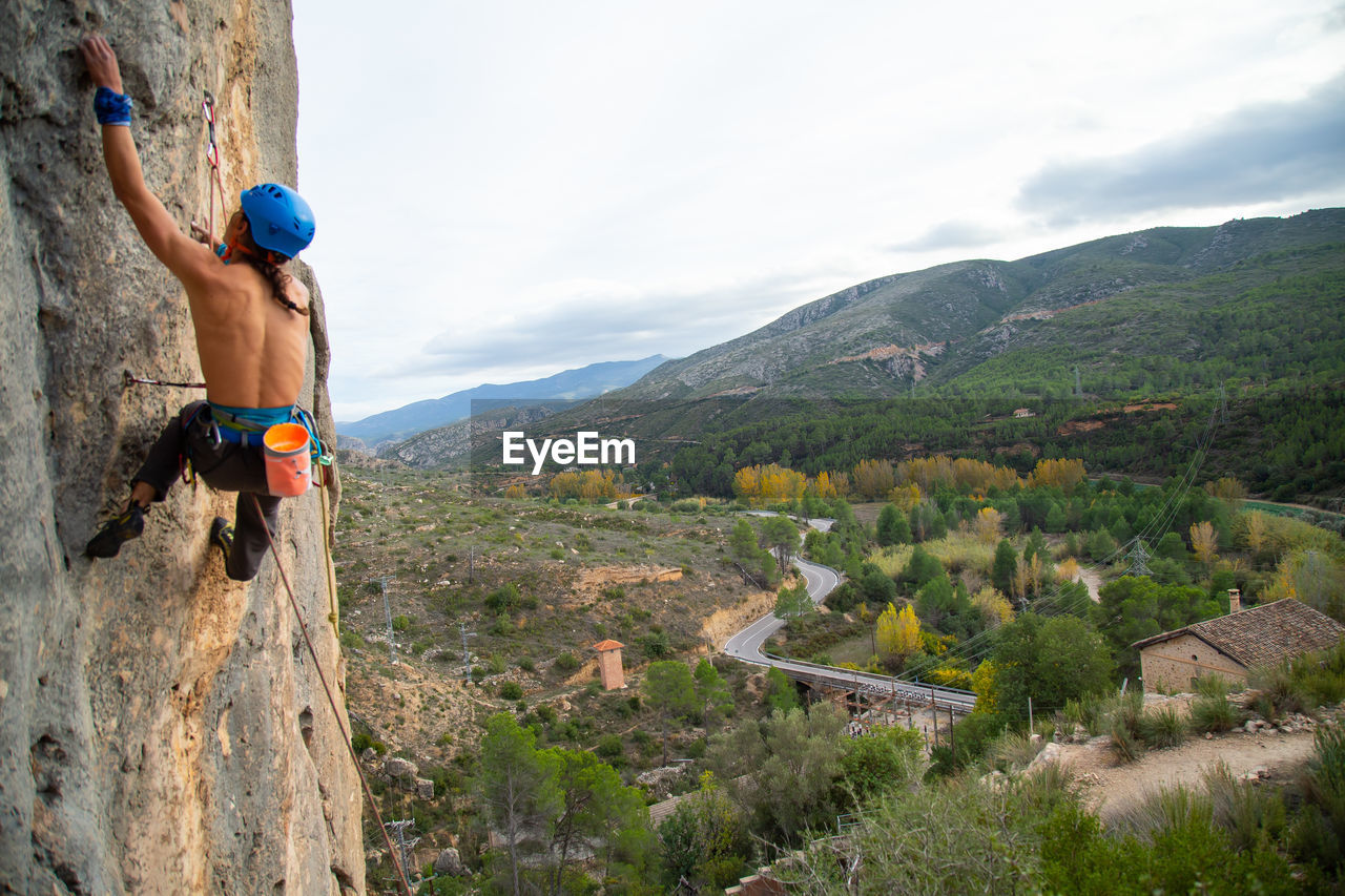 Shirtless man rock climbing against sky