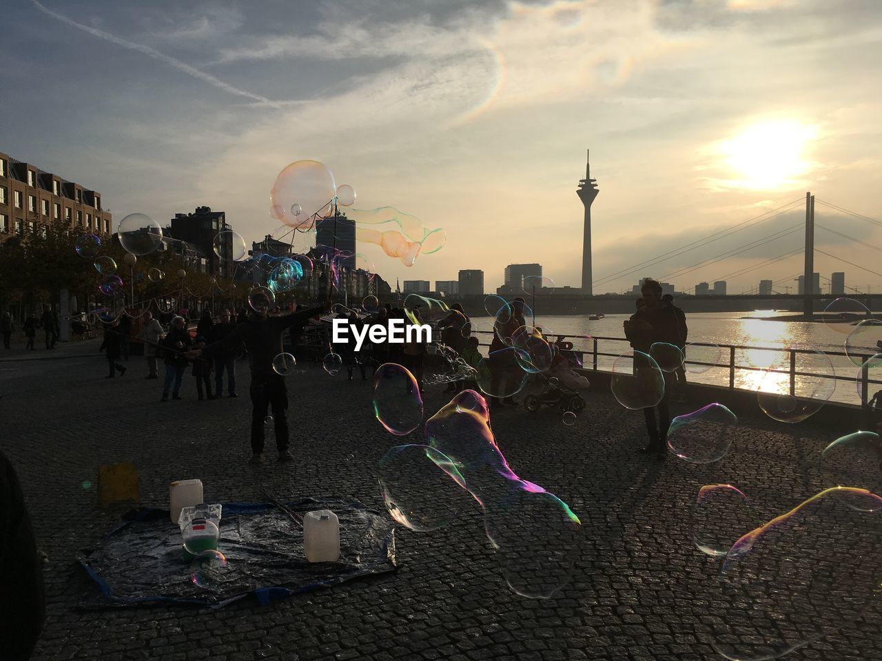 People enjoying bubbles on street with rheinturm in background during sunset