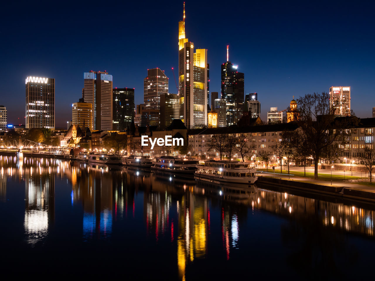 ILLUMINATED BUILDINGS BY RIVER AGAINST SKY