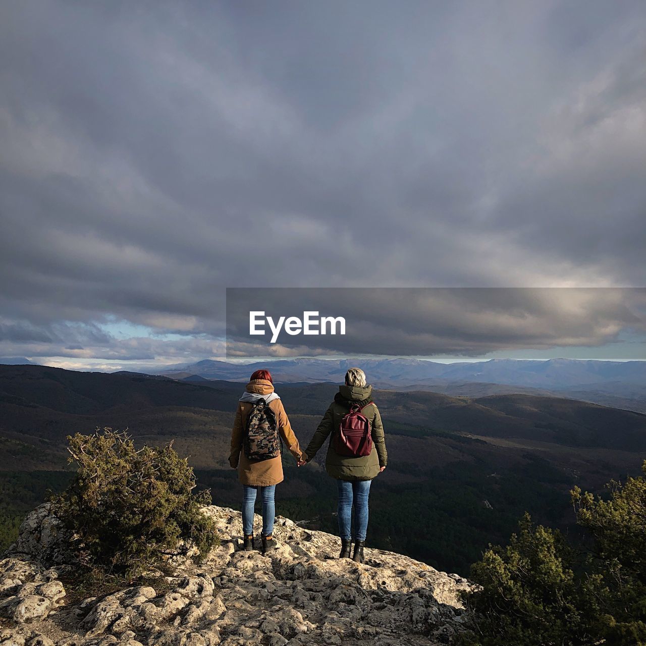 Rear view of friends standing on mountain against cloudy sky during sunset