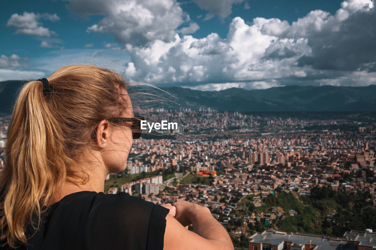 Woman looking at city buildings against cloudy sky