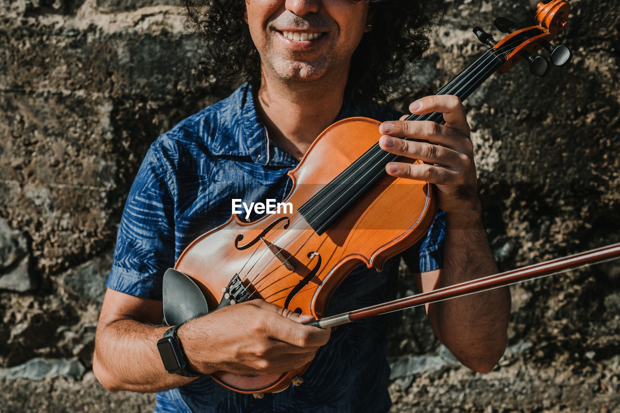 Midsection of man playing violin against wall