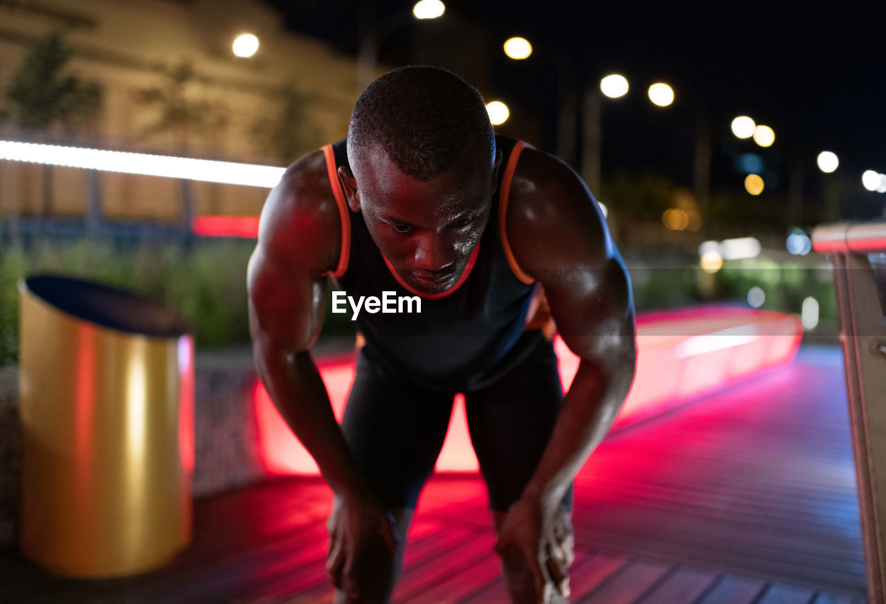 African american runner resting on night street