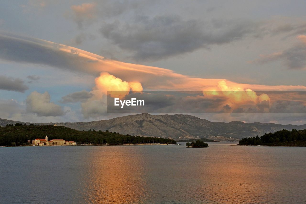 SCENIC VIEW OF SEA AGAINST MOUNTAIN DURING SUNSET