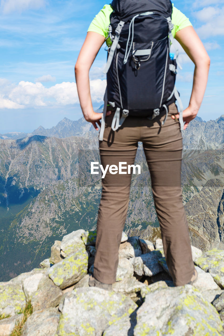 Low section of man standing on rock against sky