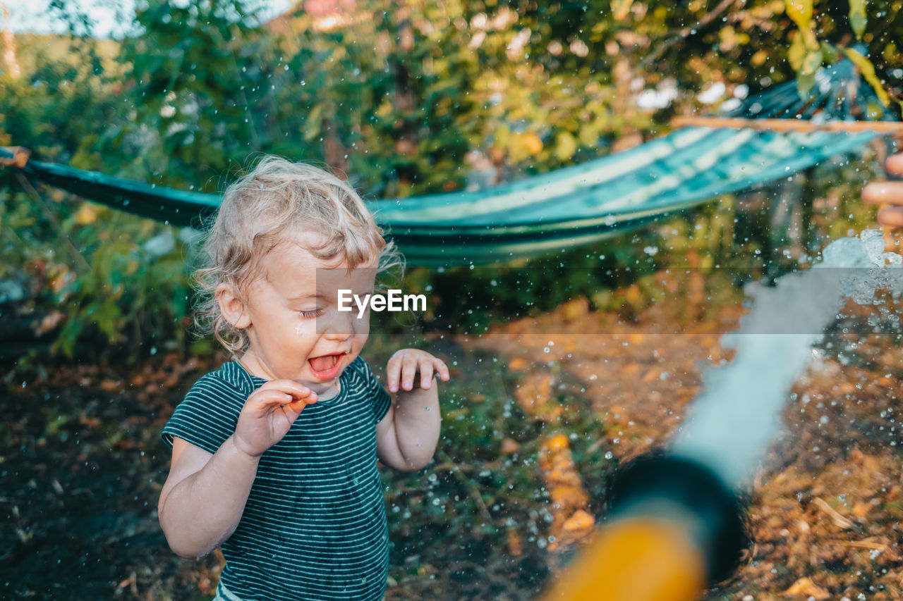 Cute boy standing at yard playing with garden hose water