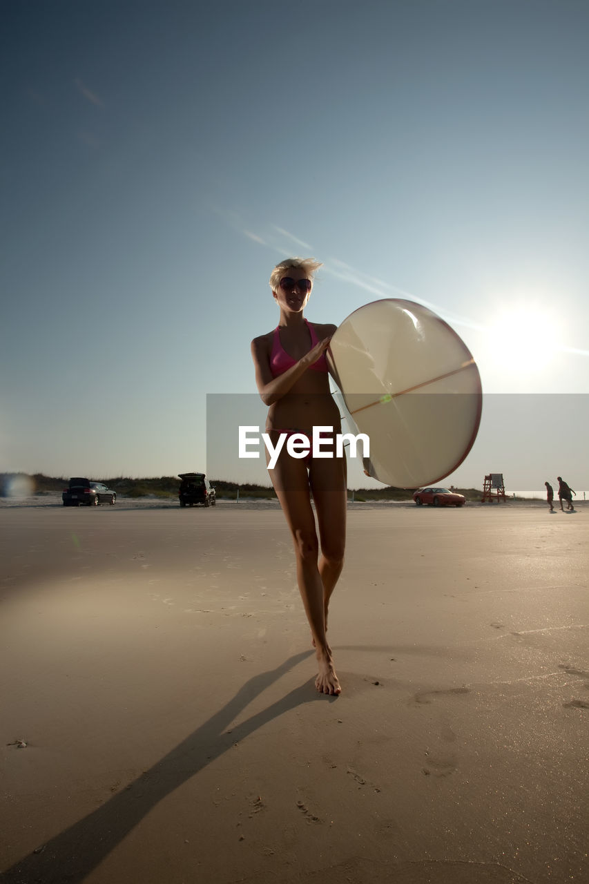 Mid adult woman with surfboard walking at beach against sky