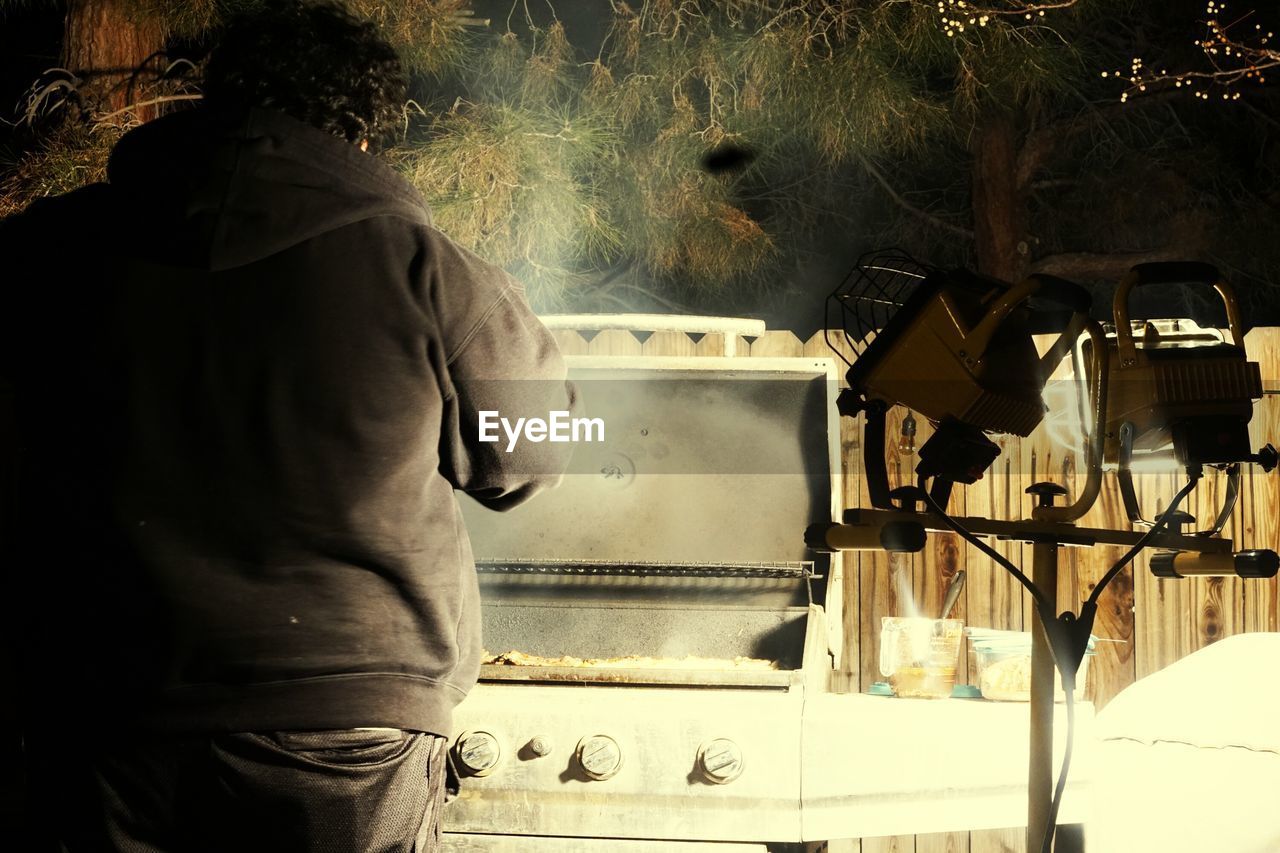 Rear view of man standing by barbecue grill at night