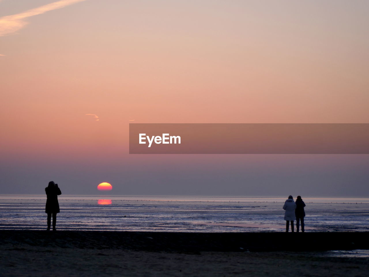 Silhouette people on beach against clear sky during sunset