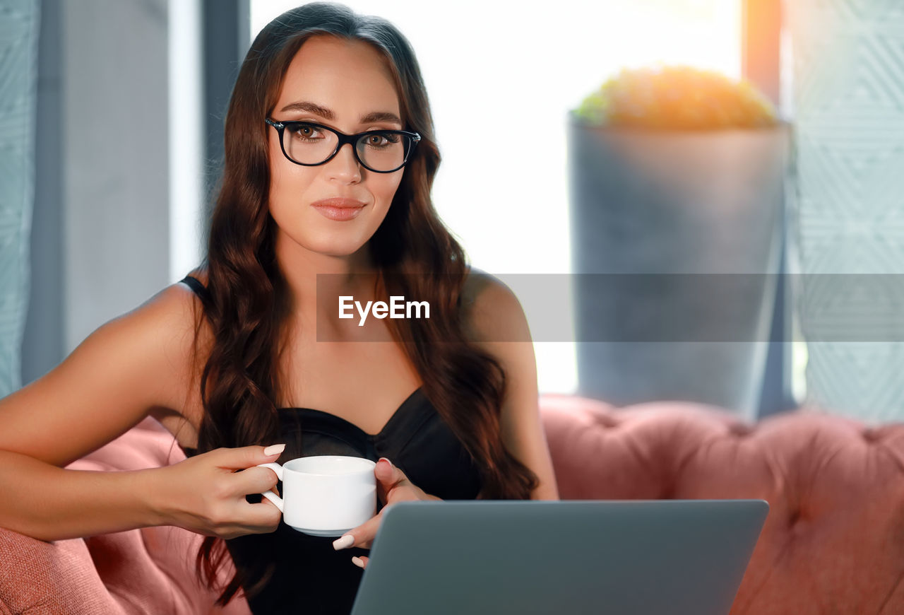 PORTRAIT OF WOMAN WITH COFFEE CUP IN LAPTOP