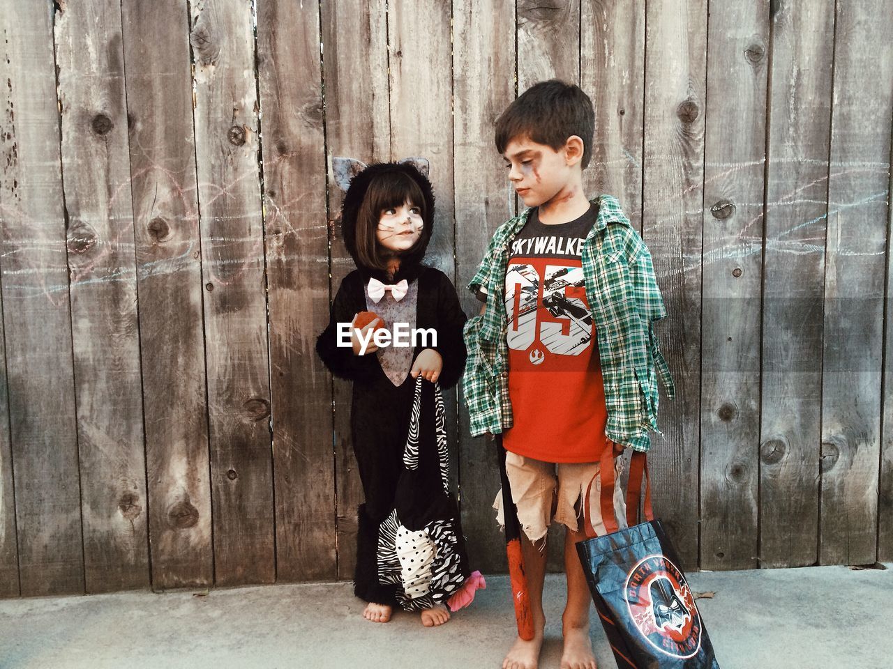 Siblings in costume standing against wooden wall during halloween