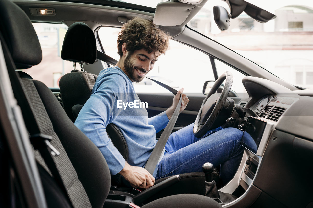 Young man fastening seat belt sitting in car