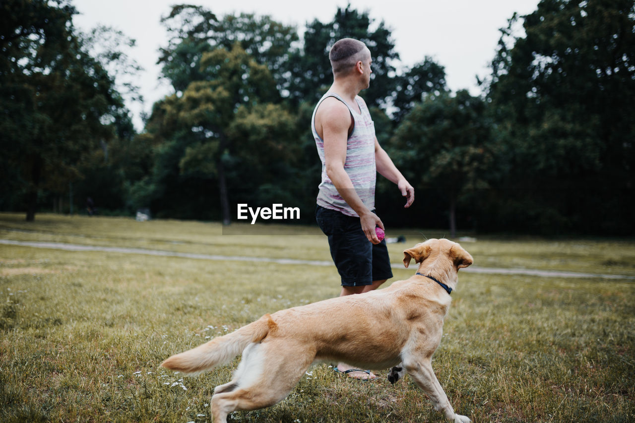 Full length of man playing with dog against trees