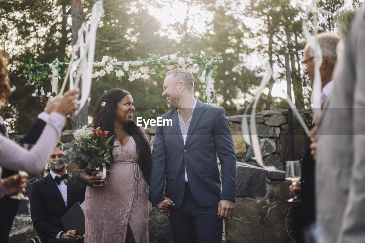 Cheerful newlywed couple holding hands while walking amidst guests at wedding ceremony