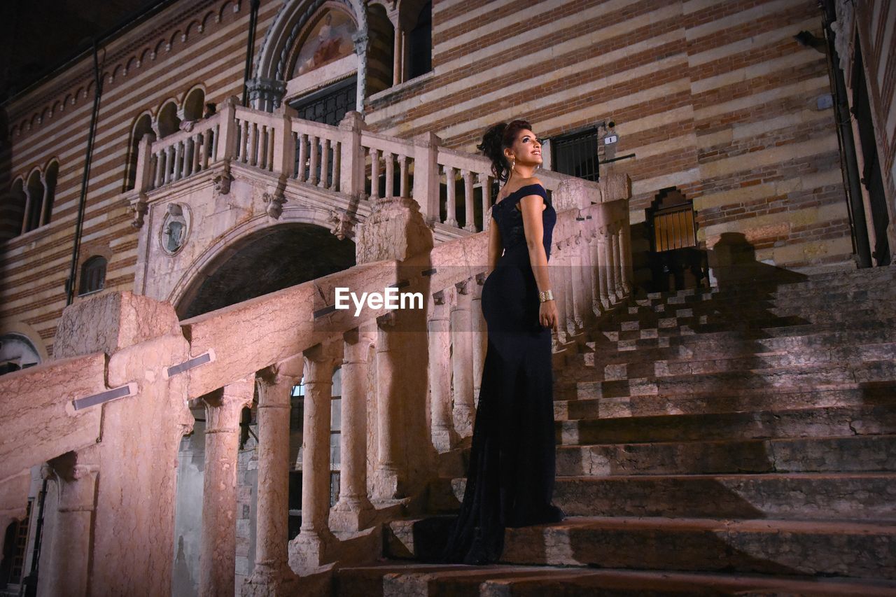 WOMAN STANDING BY RAILING AGAINST BUILDING